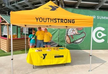 three adults under tent at baseball game